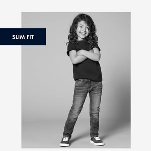 Black and white image of a young girl wearing unisex blue slim fit kids jeans
