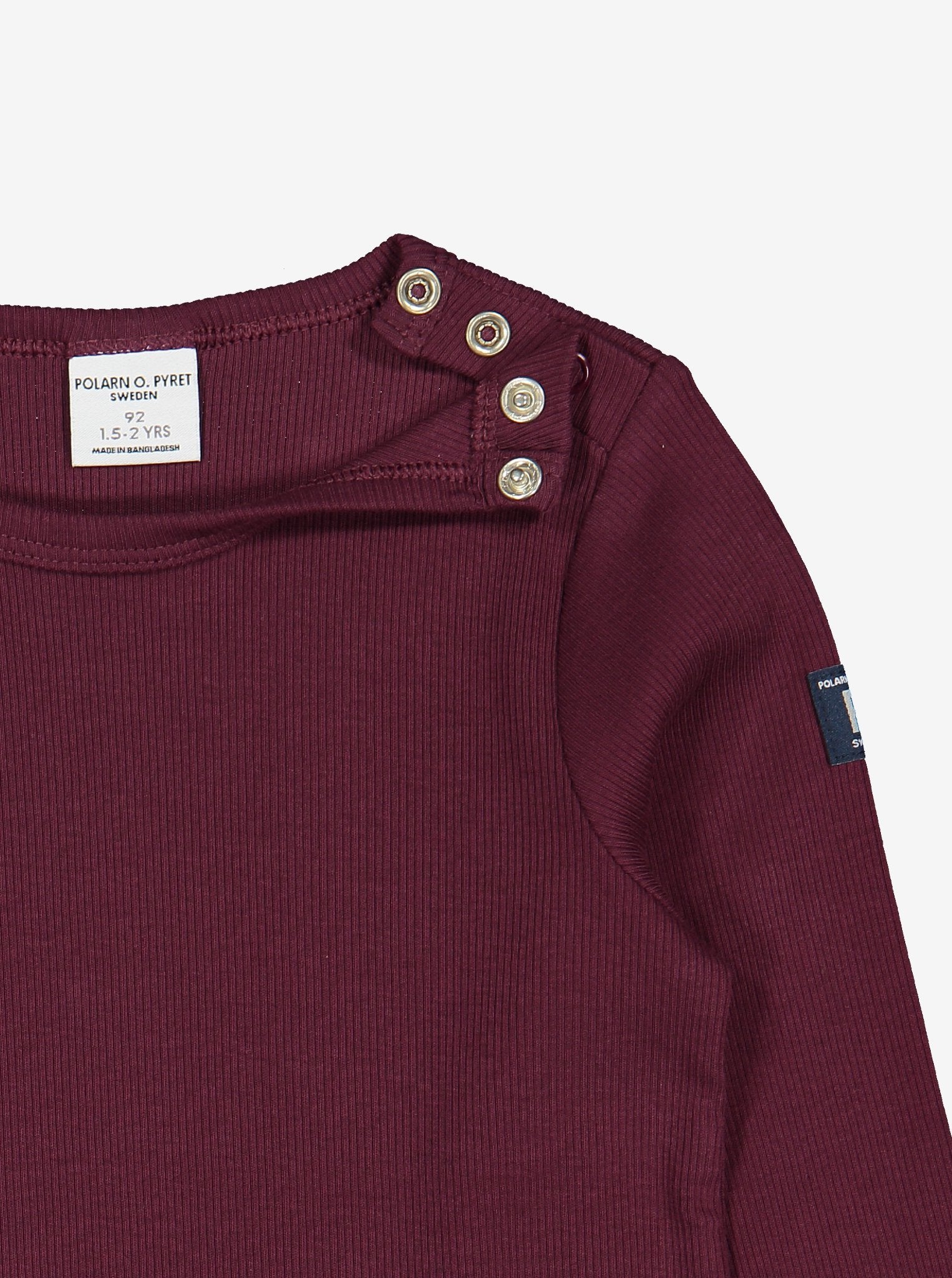 Close up view of kids burgundy red top with helpful poppers on one shoulder for easy dressing. Made in soft organic cotton