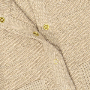Close up of unisex beige knitted cardigan in 100% organic cotton showing easy popper fastening.