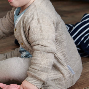 Close up of baby wearing unisex beige knitted cardigan paired with matching knitted trousers. Made in 100% organic cotton.