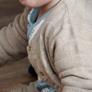 Close up of baby wearing unisex beige knitted cardigan paired with matching knitted trousers. Made in 100% organic cotton.
