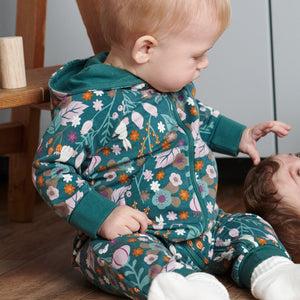 A toddler wearing a Woodland print all-in-one in GOTS organic cotton, paired with plain white cotton socks