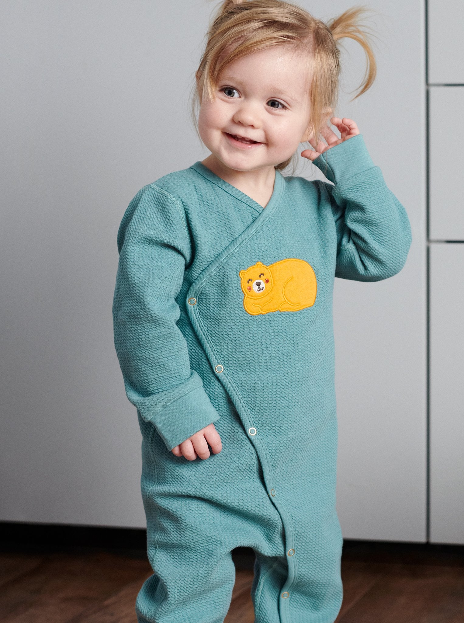 Toddler wearing wraparound onesie for newborn babies in GOTS organic cotton with adorable sleeping bear applique. With full length popper fastenings for speedy changes. Quality ribbed trim for added comfort.