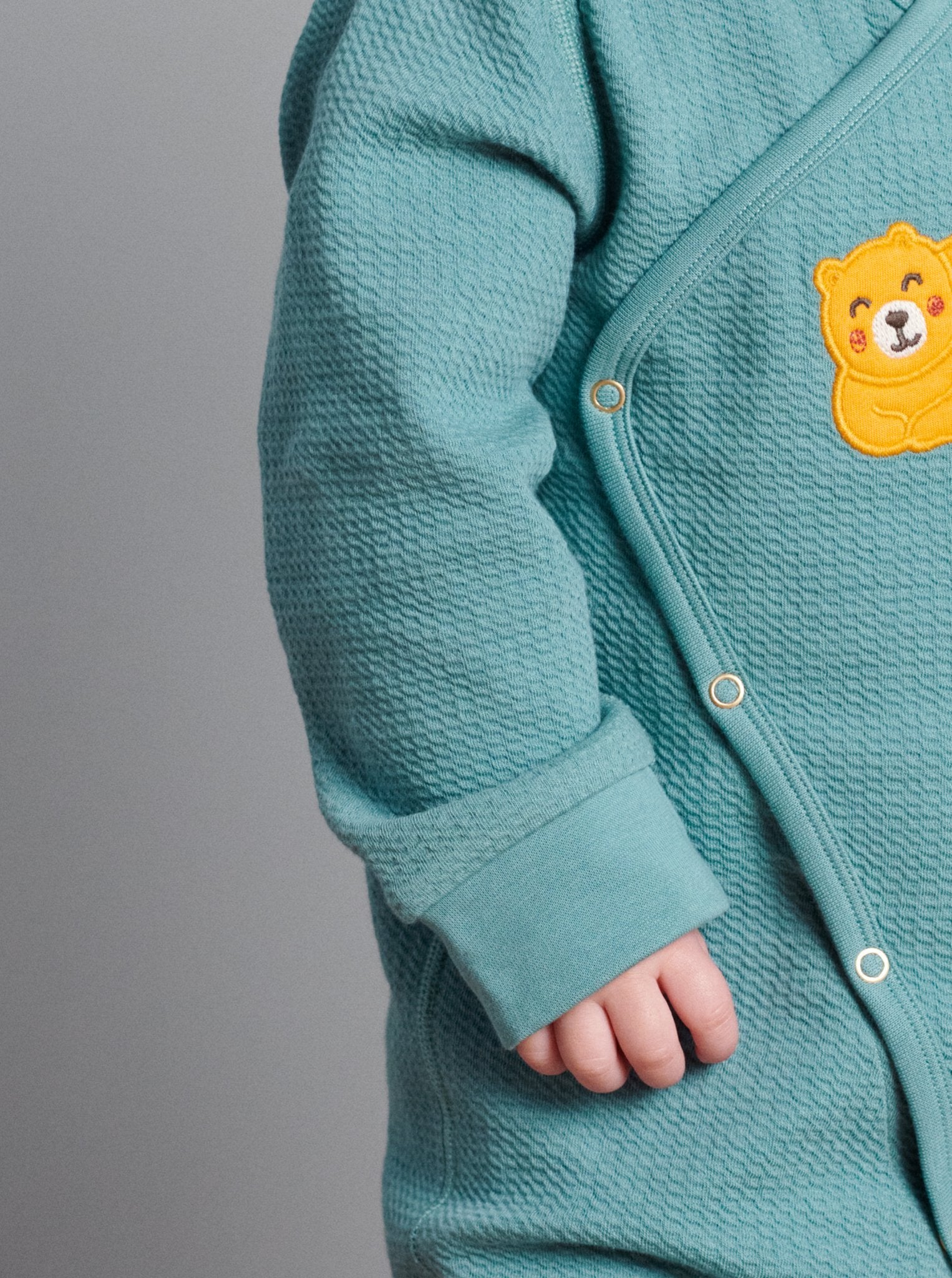 Close up of textured sleeve detail on wraparound baby onesie. Made in GOTS organic cotton with adorable sleeping bear applique