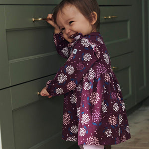 A baby girl wearing PO.P's sustainable purple floral baby dress made of organic cotton, playing with kitchen drawers