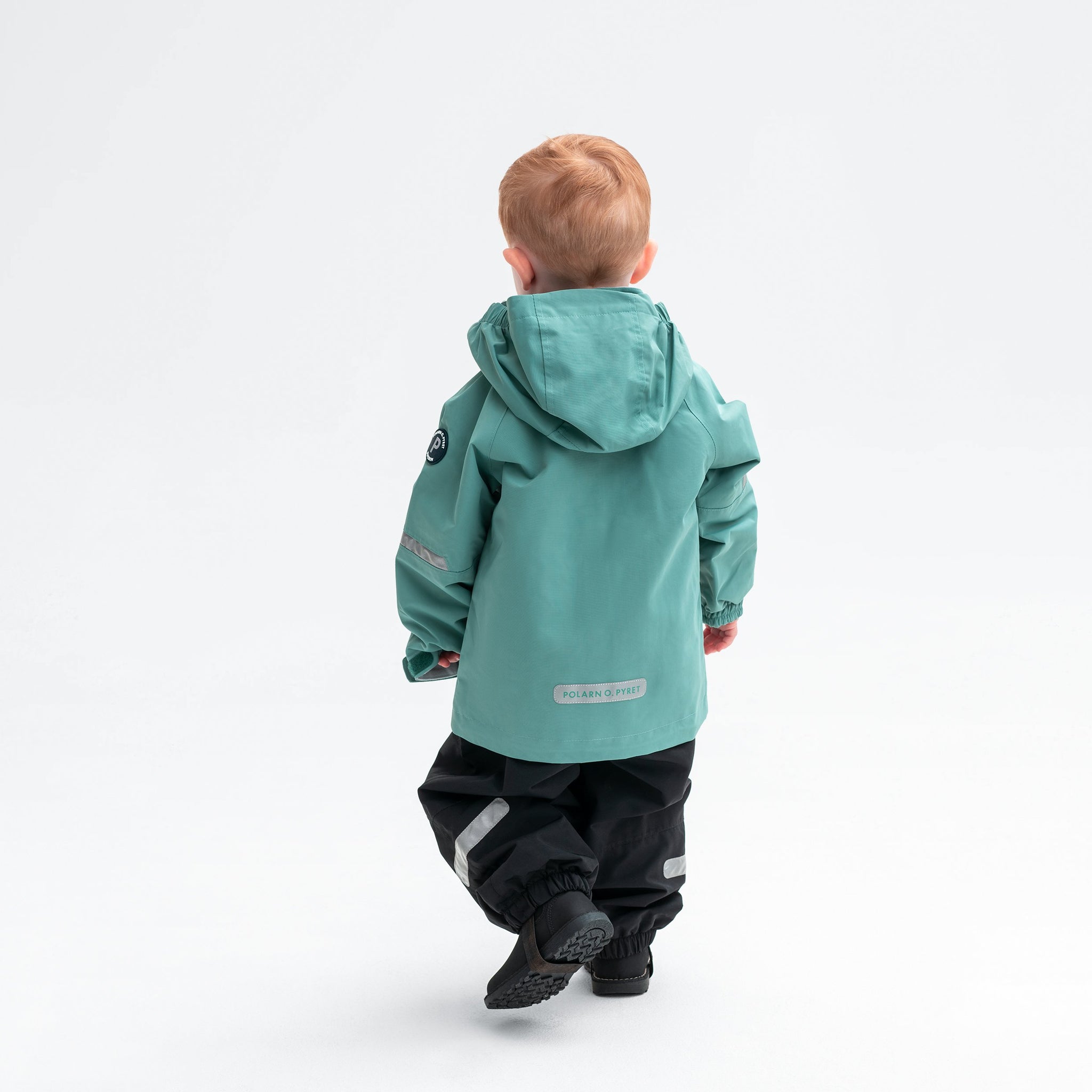 A little boy wearing a green kids waterproof shell jacket with hood, made from eco-friendly water repellent technology.