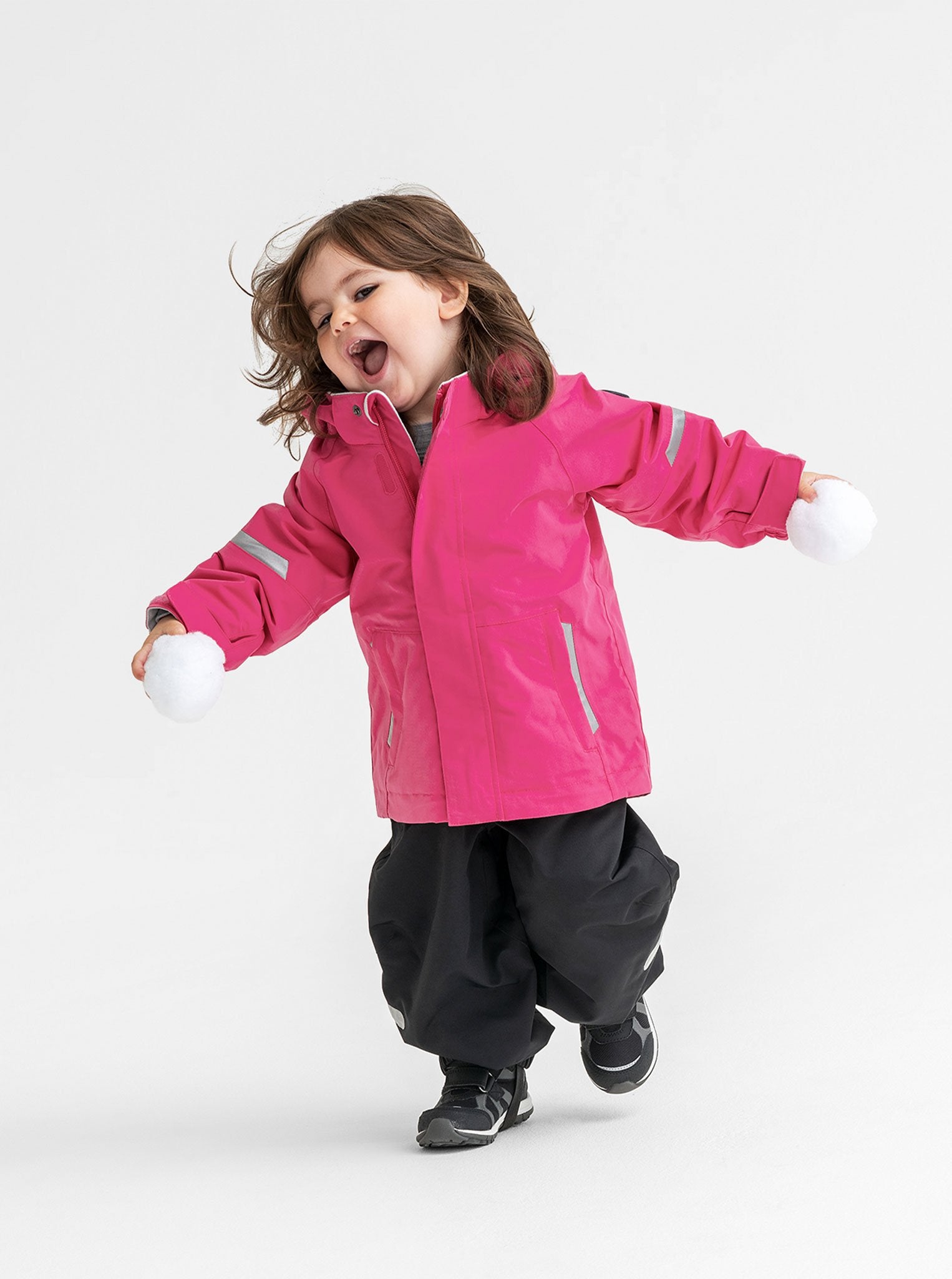 A young girl wearing a pink, toddlers waterproof jacket, paired with black, kids waterproof trousers, made of shell fabric.