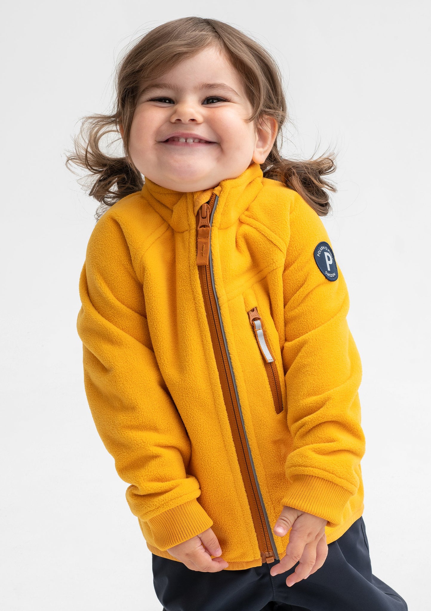 A smiling toddler wearing a yellow, kids waterproof fleece jacket, made of soft and breathable fabric, with zip reflectors.