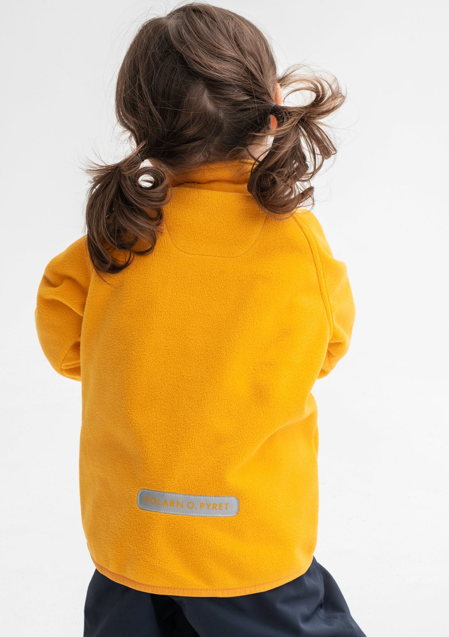 Back view of a young girl wearing a yellow, kids waterproof fleece jacket with cuff thumbholes, made of lightweight fabric.