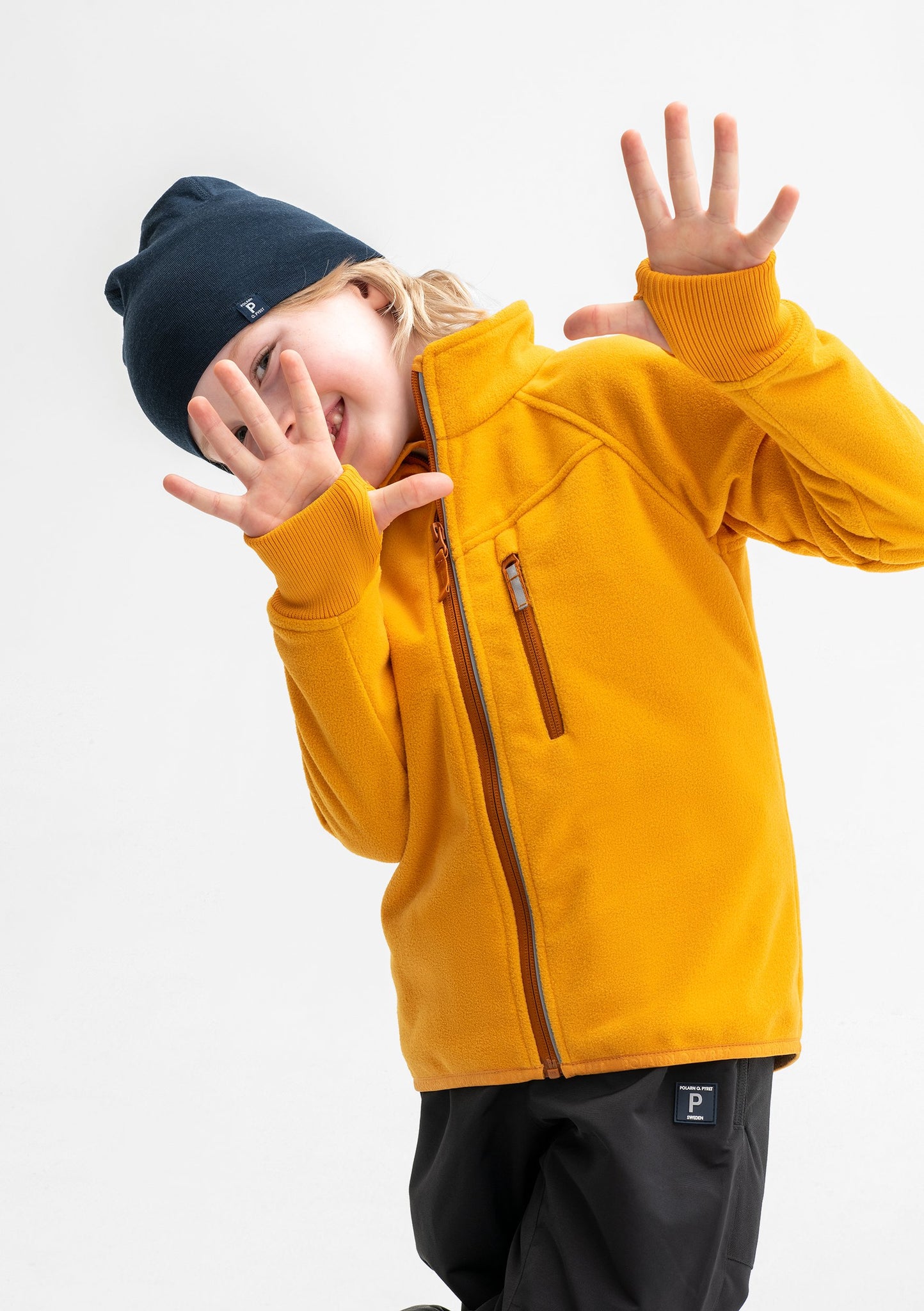 A young boy sporting a yellow, kids waterproof fleece jacket, paired with a navy, kids merino wool beanie.
