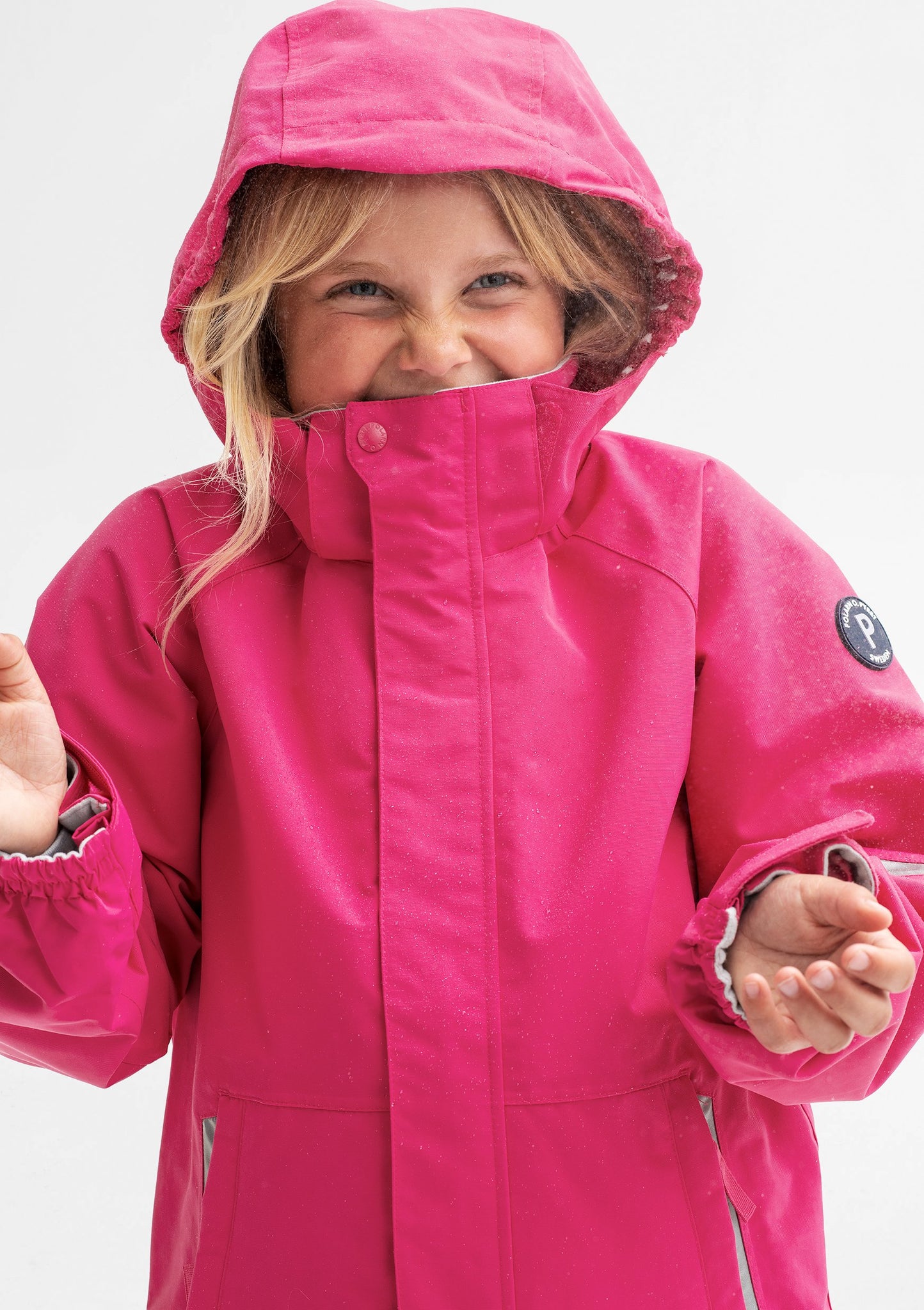 A young girl wearing a pink, kids waterproof jacket with detachable hood and adjustable cuffs, made of soft shell fabric.