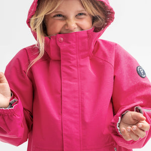 A young girl wearing a pink, kids waterproof jacket with detachable hood and adjustable cuffs, made of soft shell fabric.