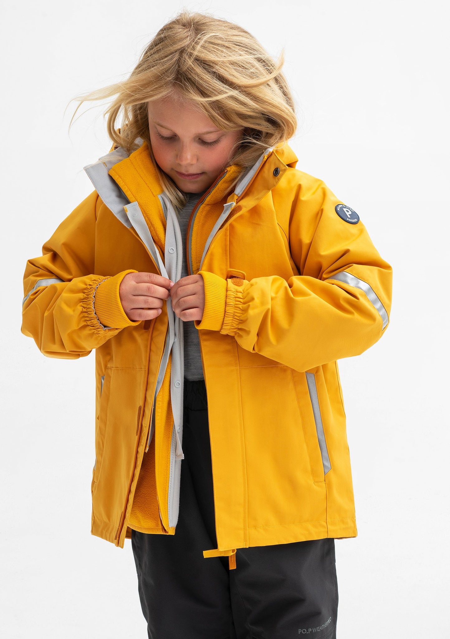A young girl wearing a yellow, kids waterproof shell jacket paired with a yellow, kids waterproof fleece jacket.