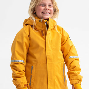 A young girl wearing a yellow waterproof jacket for kids, includes a detachable hood, front pockets and reflectors.