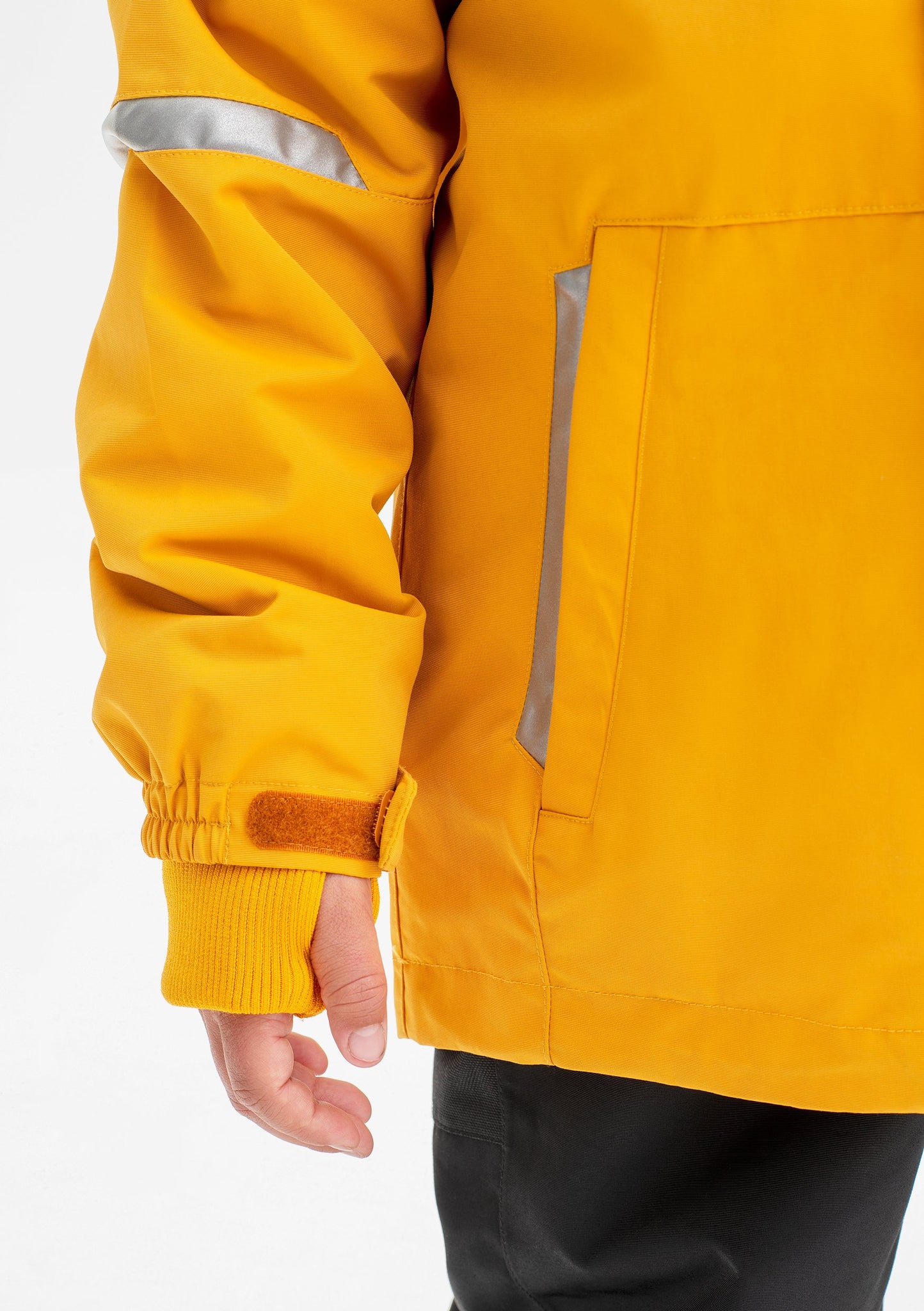 Close up shot of the pocket and adjustable cuff of a yellow, kids waterproof jacket, made of lightweight shell fabric.