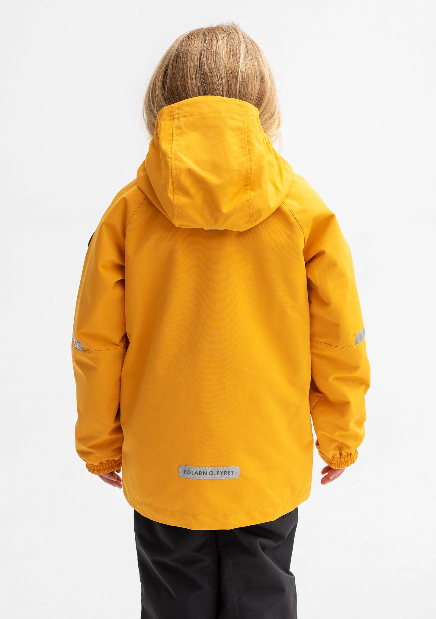 Back view of a young girl wearing a yellow, kids waterproof jacket with detachable hood and reflectors, made of shell fabric.