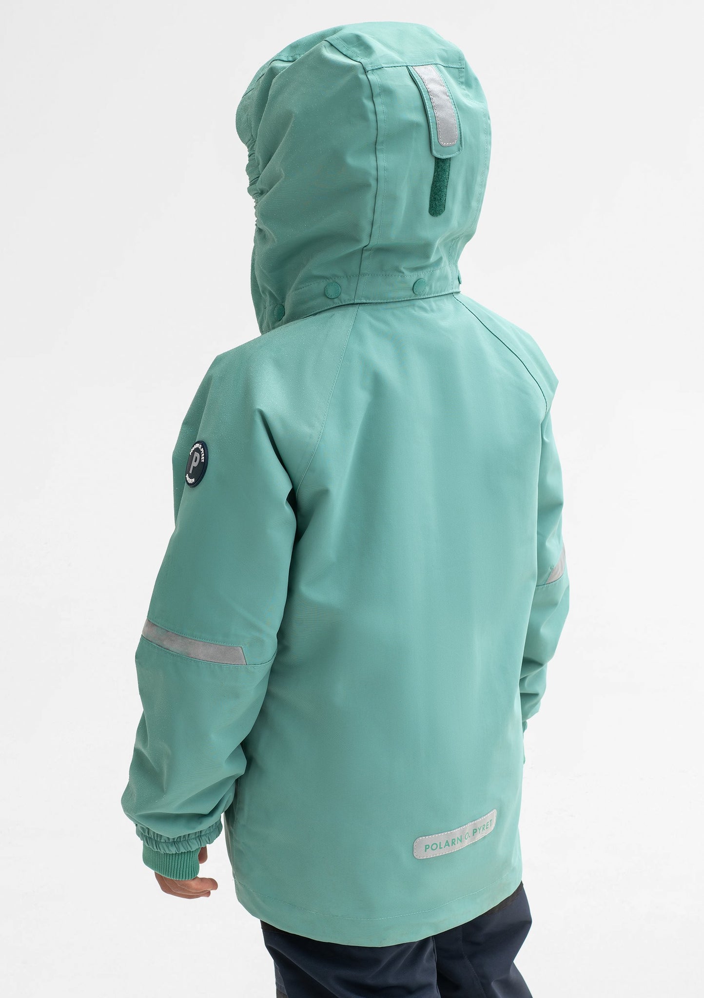 Back view of a boy wearing a green, kids waterproof jacket made of lightweight fabric, with silver reflectors on the sleeves.
