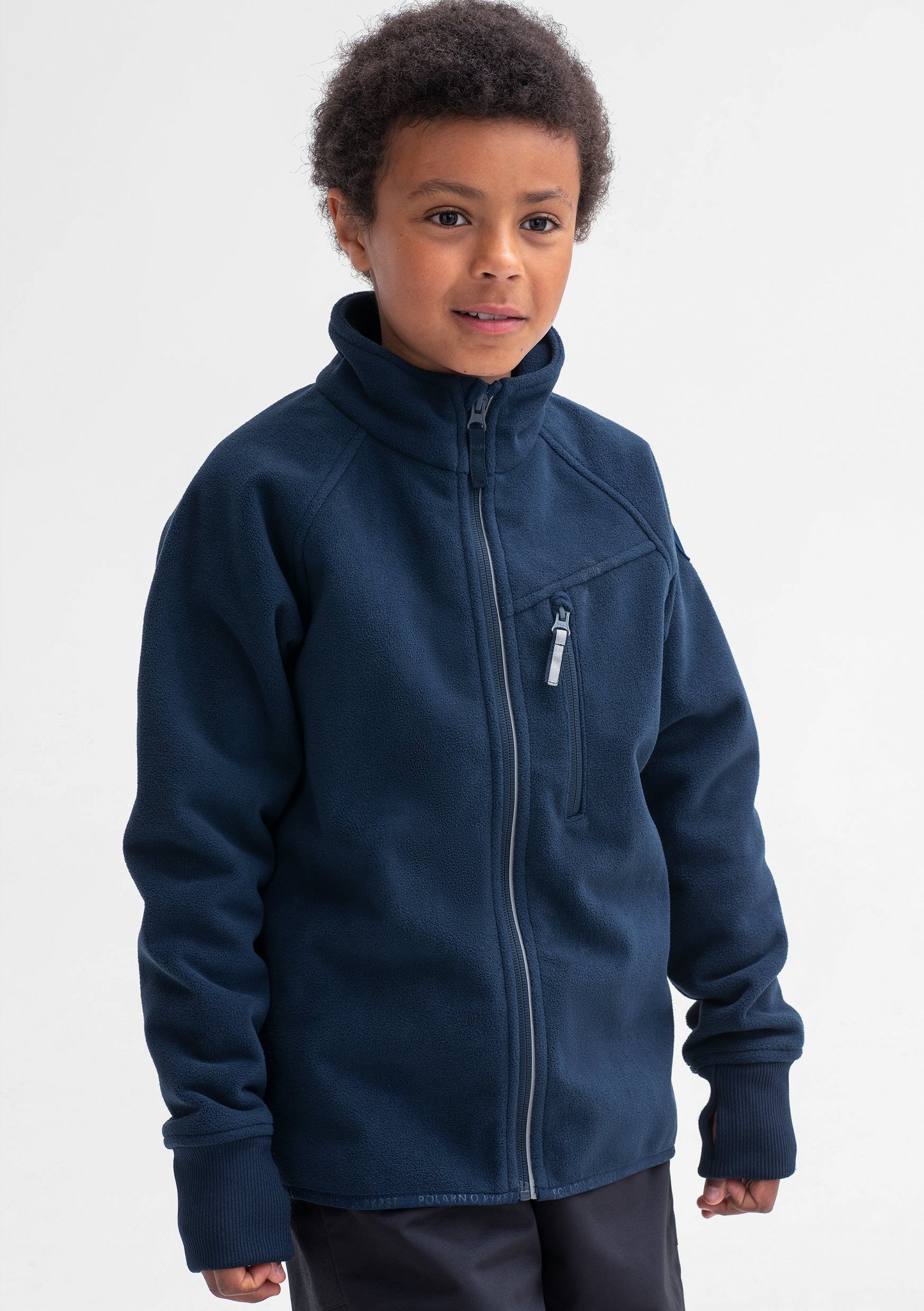 A boy wearing a navy, kids fleece jacket with reflectors on zips, front pocket & cuff thumbholes, made of soft fabric.