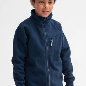 A boy wearing a navy, kids fleece jacket with reflectors on zips, front pocket & cuff thumbholes, made of soft fabric.