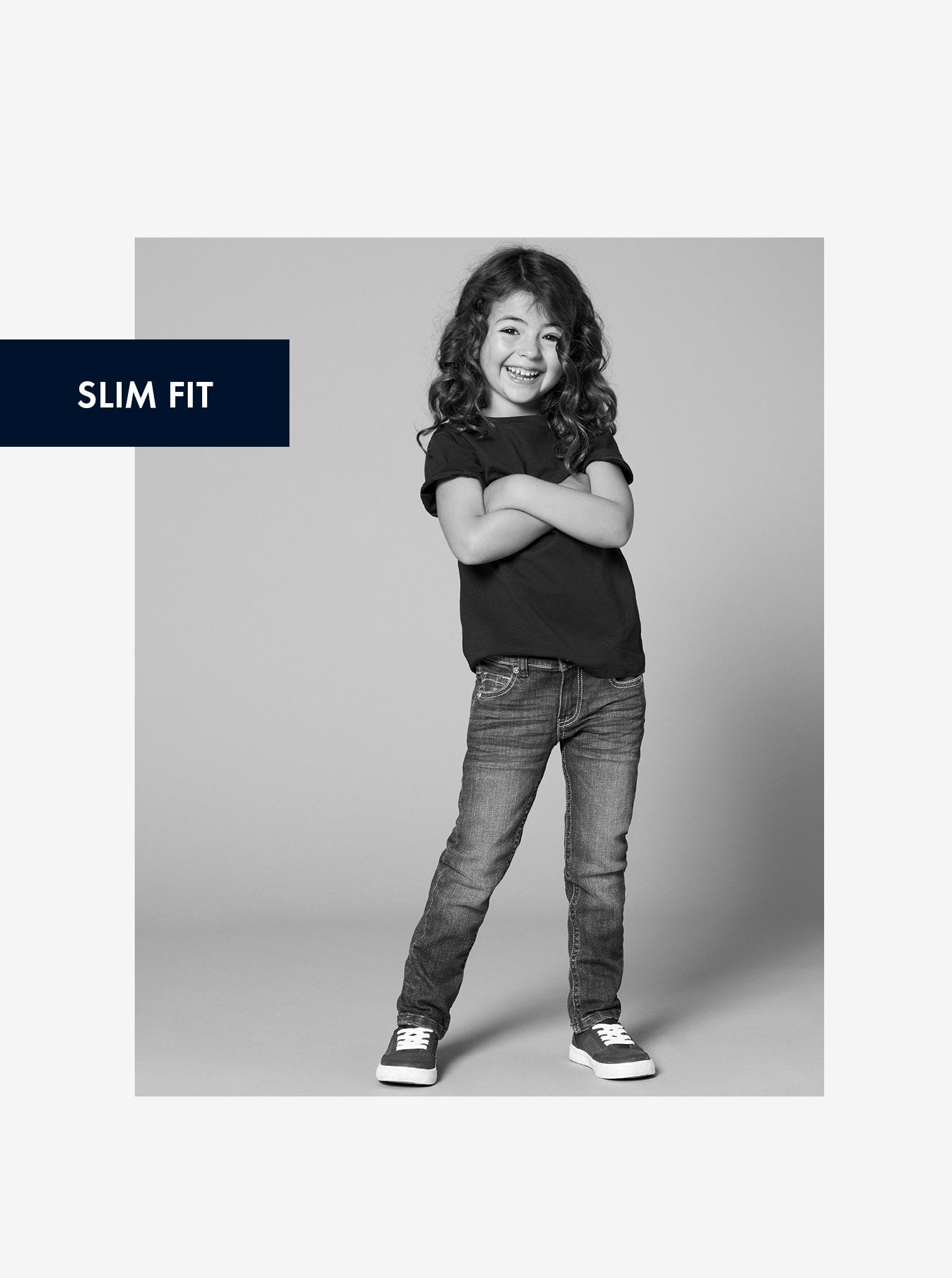 Black and white image of a young girl wearing unisex blue slim fit kids jeans