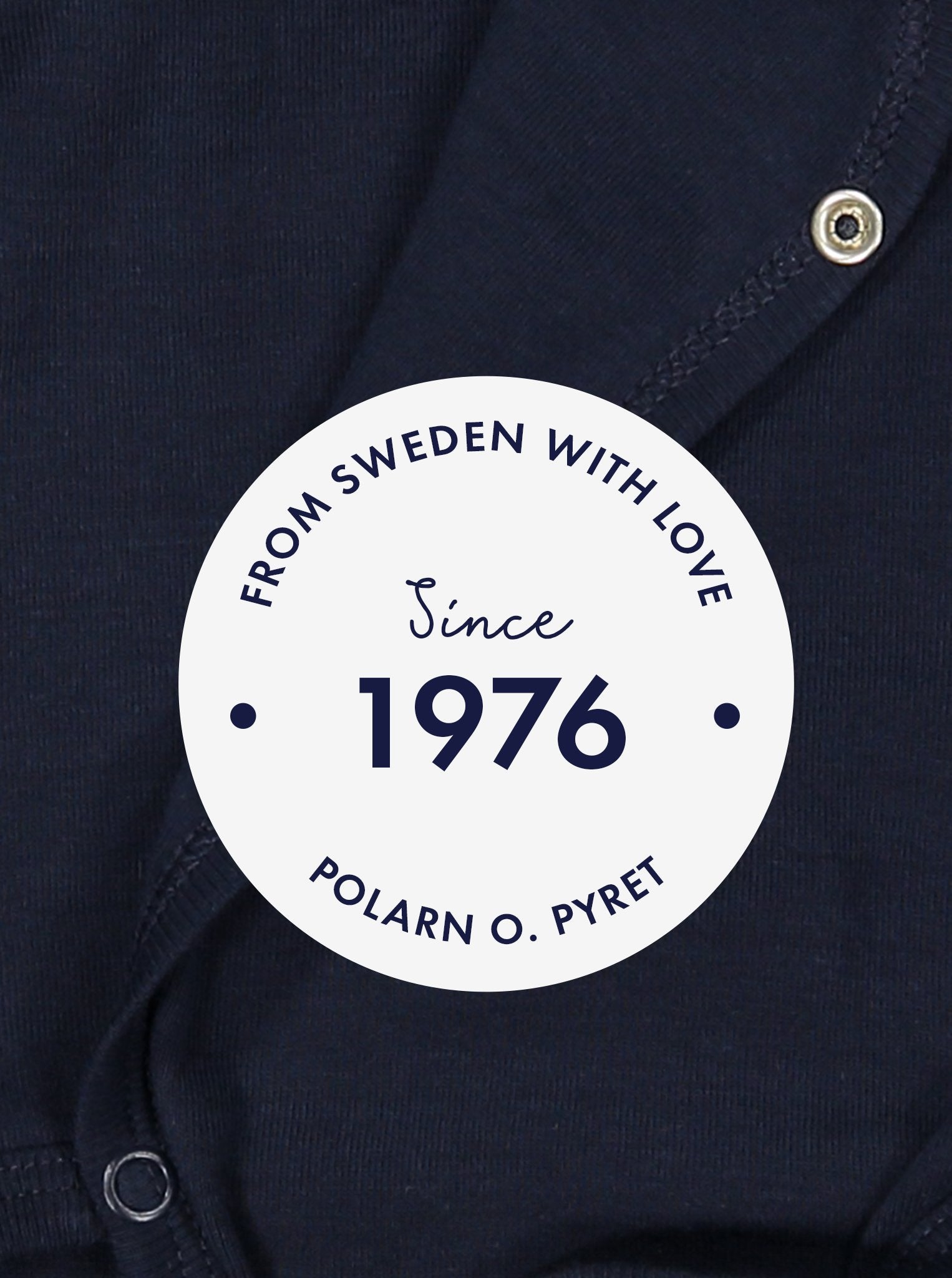 White round label with the text 'From Sweden With Love, Since 1976" shown in front of a navy blue babygrow background.